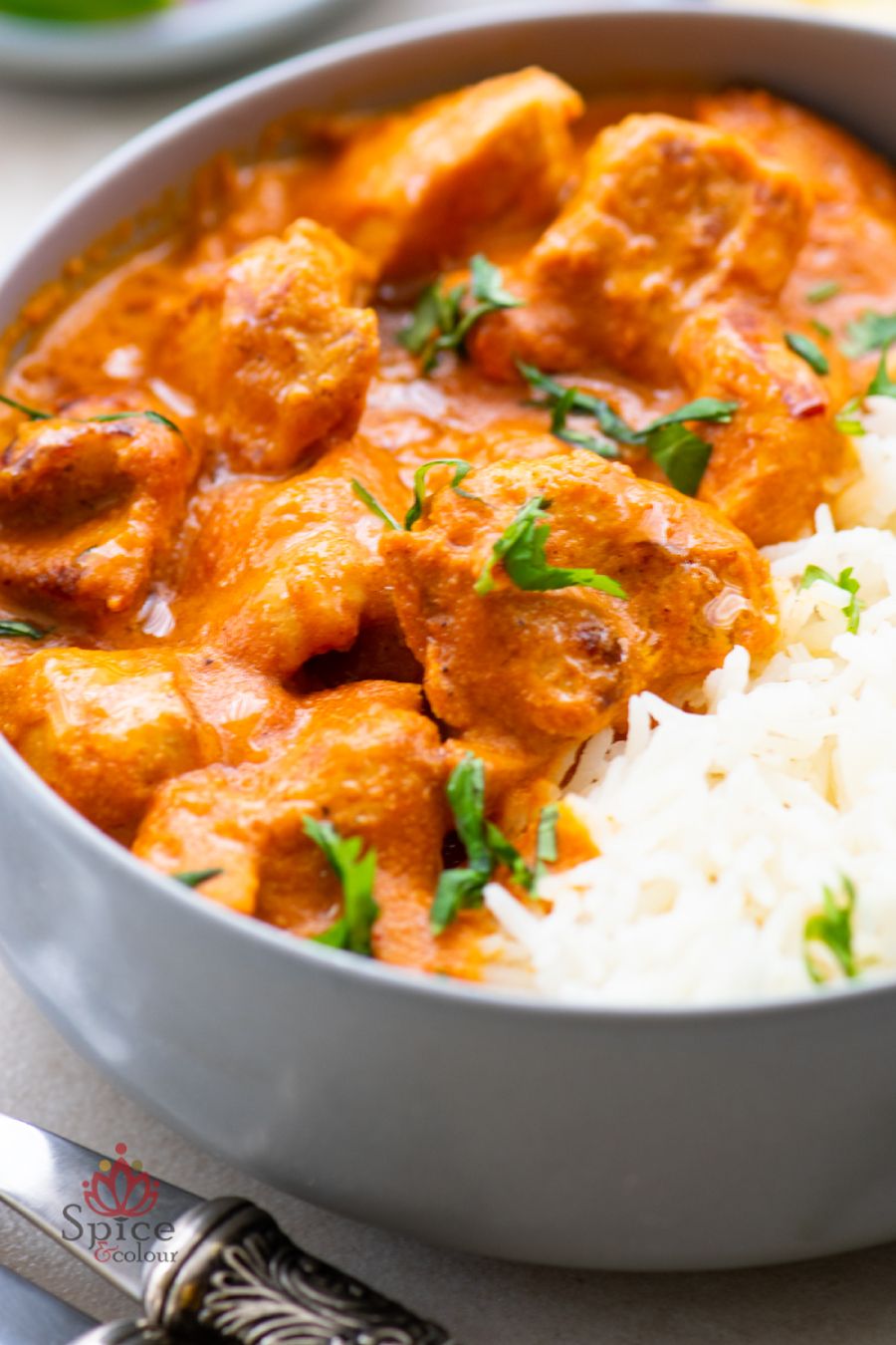 Butter Chicken servido con arroz basmati, cubierto con crema y hojas de cilantro.